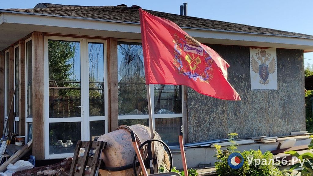 Флаг Оренбургской области на фоне пострадавшего во время паводка дома, Оренбург